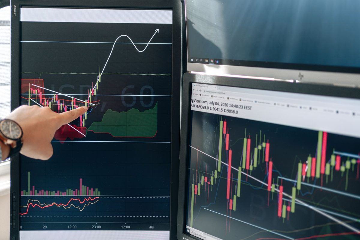 A person pointing at charts on dual monitors in a modern workspace