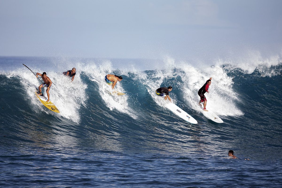 Surfers riding a wave in Paea, Tahiti